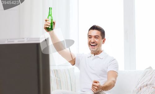 Image of smiling man watching tv and drinking beer at home