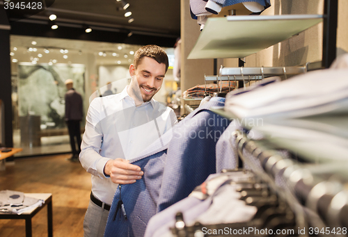 Image of happy young man choosing clothes in clothing store