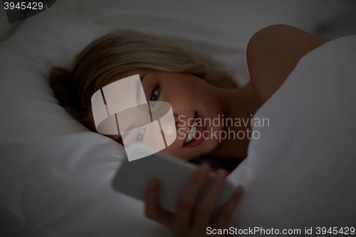 Image of young woman with smartphone in bed at home bedroom