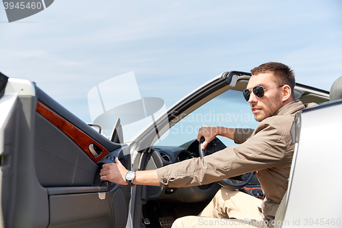 Image of happy man opening door of cabriolet car outdoors