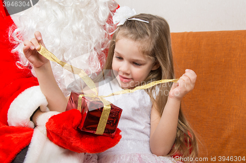 Image of Girl unleashes a red ribbon gift in the hands of Santa Claus