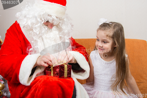 Image of Santa Claus helps to untie the ribbon gift, little girl happily looking at him