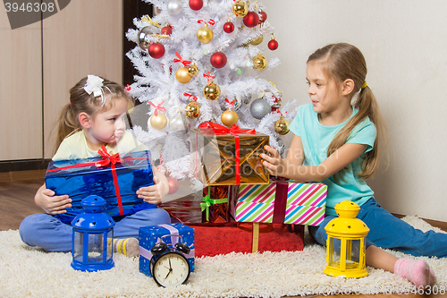 Image of Two girls share presented New Year gifts at the Christmas tree