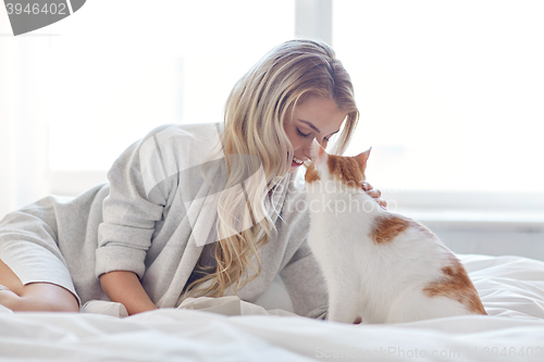 Image of happy young woman with cat in bed at home