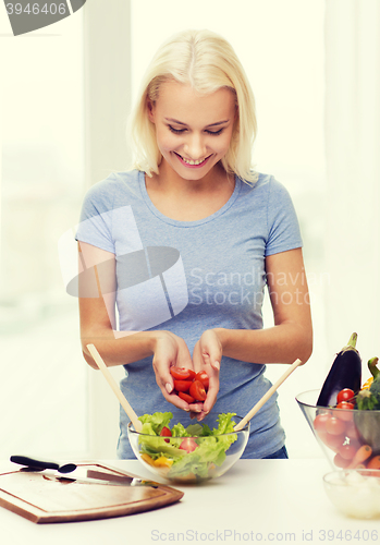 Image of smiling woman cooking vegetable salad at home