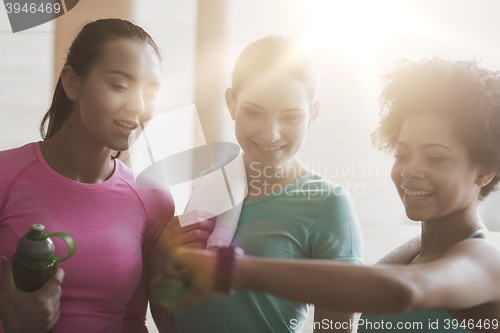 Image of happy women showing time on wrist watch in gym