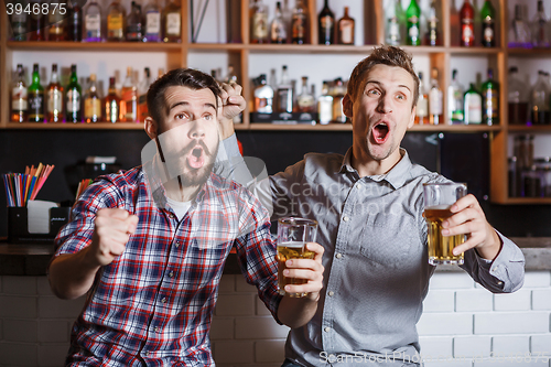 Image of Young people with beer watching football in a bar