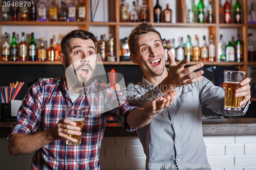 Image of Young people with beer watching football in a bar