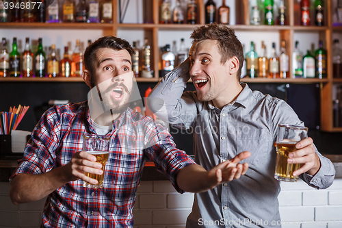 Image of Young people with beer watching football in a bar