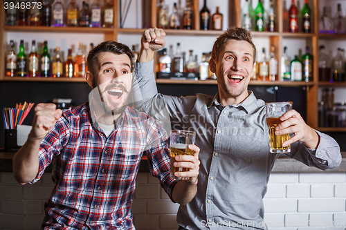 Image of Young people with beer watching football in a bar