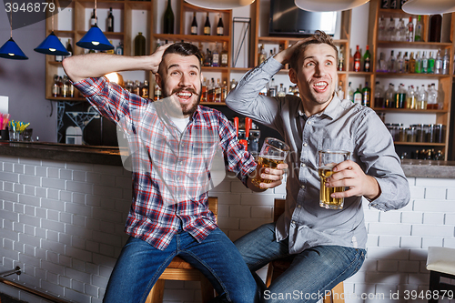 Image of Young people with beer watching football in a bar