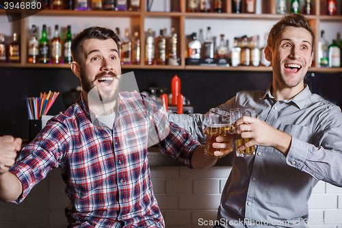 Image of Young people with beer watching football in a bar