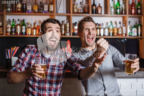 Image of Young people with beer watching football in a bar