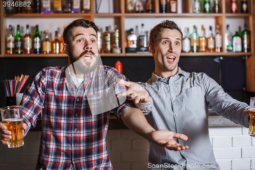 Image of Young people with beer watching football in a bar