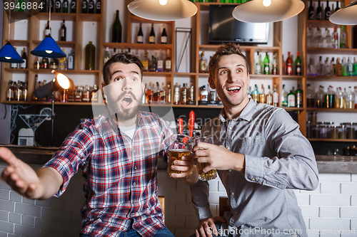 Image of Young people with beer watching football in a bar