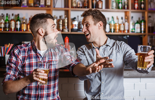 Image of Young people with beer watching football in a bar