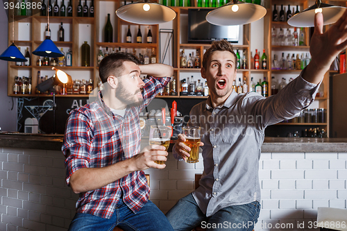 Image of Young people with beer watching football in a bar