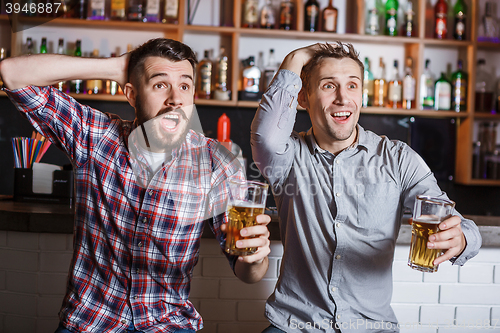 Image of Young people with beer watching football in a bar