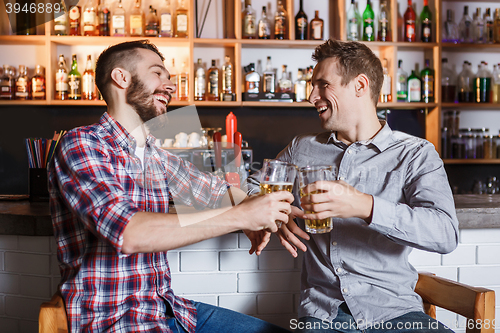 Image of Happy friends drinking beer at counter in pub