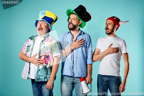 Image of The three football fans singing the national anthem over blue