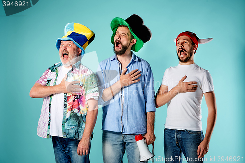 Image of The three football fans singing the national anthem over blue