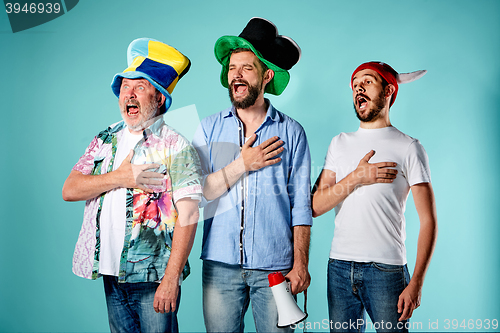 Image of The three football fans singing the national anthem over blue