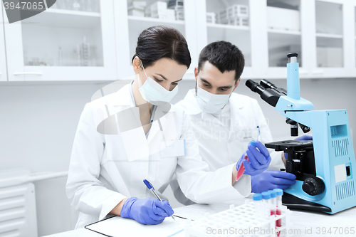 Image of scientists with clipboard and microscope in lab