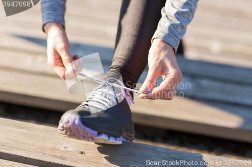 Image of close up of sporty woman tying shoelaces outdoors