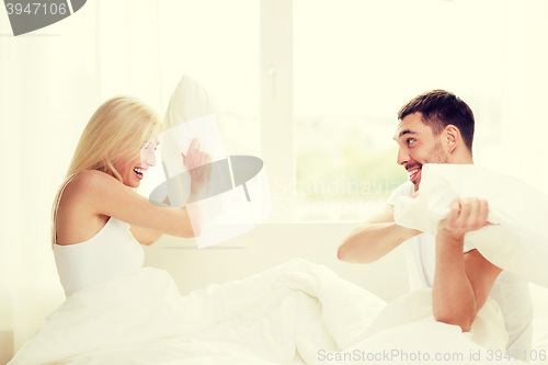 Image of happy couple having pillow fight in bed at home