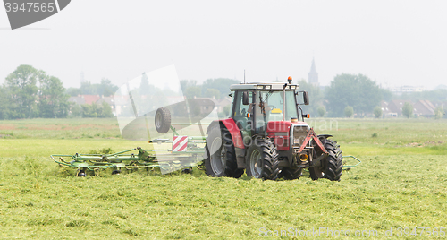 Image of Farmer uses tractor to spread hay on the field