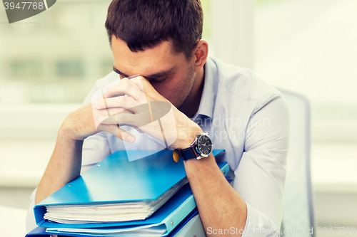 Image of sad businessman with stack of folders at office