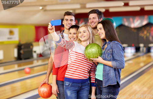 Image of happy friends with smartphone in bowling club