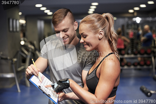 Image of smiling woman with trainer and clipboard in gym