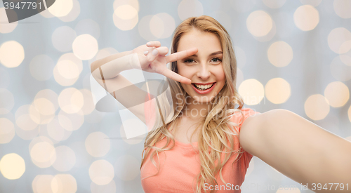 Image of smiling woman taking selfie and showing peace sign