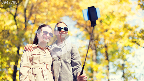 Image of happy girls with smartphone selfie stick