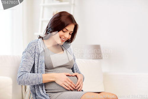 Image of happy pregnant woman making heart gesture at home