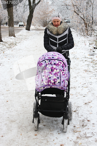 Image of Woman with baby in perambulator walking in winter 