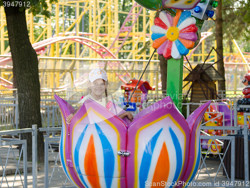 Image of Six-year girl riding on a carousel, sitting in a stylized floret