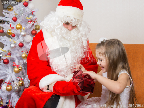 Image of Little girl joyfully opens a gift that keeps grandfather frost