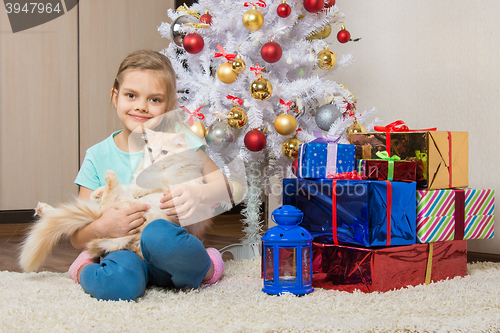 Image of Joyful seven year old girl with a cat sitting under the Christmas tree with gifts