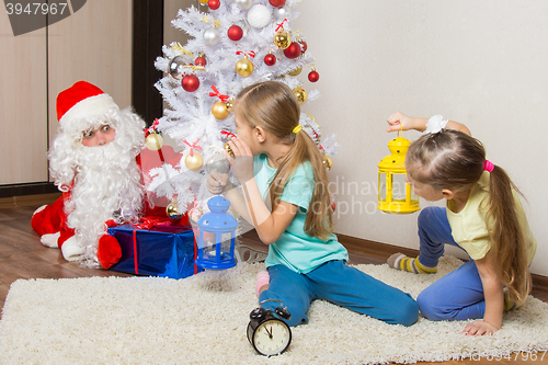 Image of Two girls with flashlights to see Santa Claus who was trying to discreetly put the presents under the Christmas tree