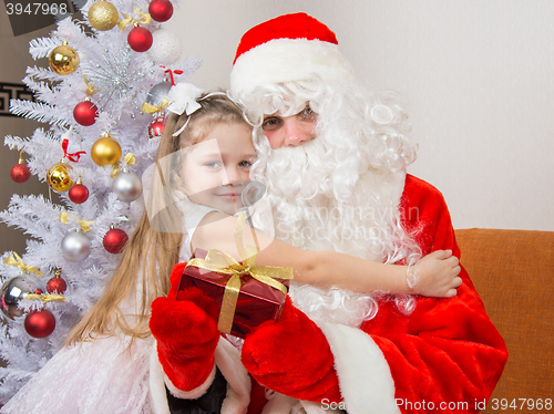 Image of Little girl hugging Santa Claus which is holding a gift