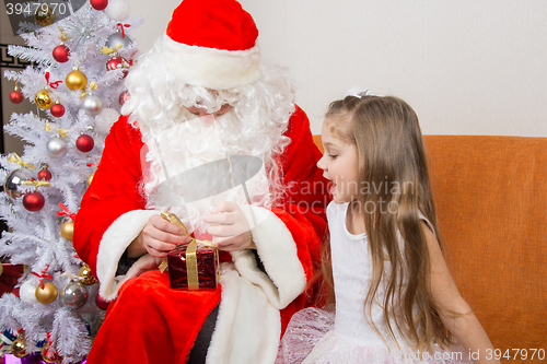 Image of The girl with interest looks like Father Christmas helps to open her gift