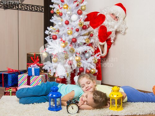 Image of Santa Claus peeking out of a tree in front of which the two girls sleeping mat