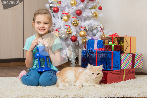 Image of Seven-year girl sits with a cat under the Christmas tree with gifts and smiling happily