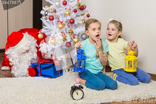 Image of Two girls with flashlights dreaming of gifts on New Years night, and Santa Claus put presents under the Christmas tree