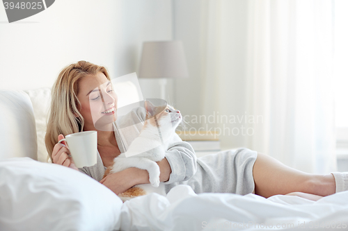 Image of happy woman with coffee and cat in bed at home