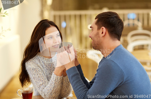 Image of happy couple with tea holding hands at restaurant