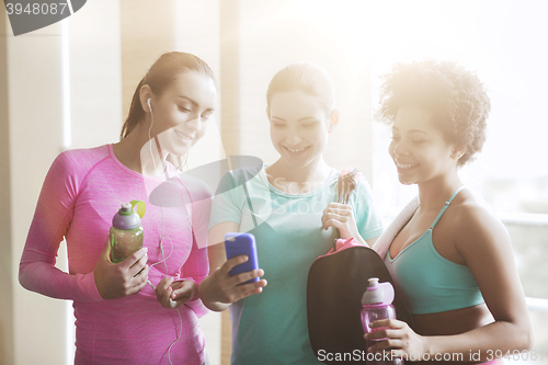 Image of happy women with bottles and smartphone in gym