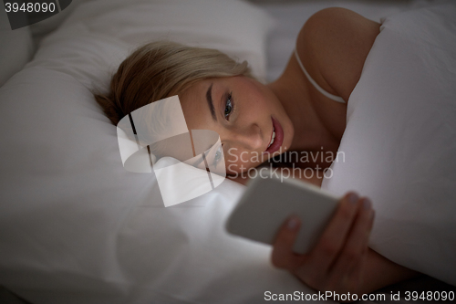 Image of young woman with smartphone in bed at home bedroom